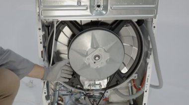 Tamirci, bozuk çamaşır makinesinin kayışını yavaşça çıkarıyor..