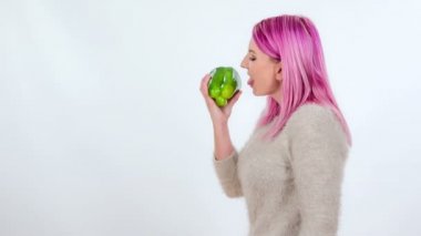 Pembe saçlı genç bir kadın yeşil biberi ısırıyor..