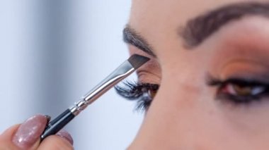 A make up artist shapes the client's eyebrows and she puts on some darker colour.