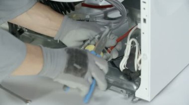 Reapman çamaşır makinesinin eletric kısmındaki plastik tüpü yavaşça çıkarıyor. Özel bükülmüş burun kerpeteni için yardım ediyor..