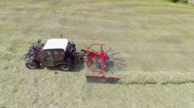 Bir traktör saman hazırlarken tarımsal makineleri çekiyor. Hava görüntüsü.