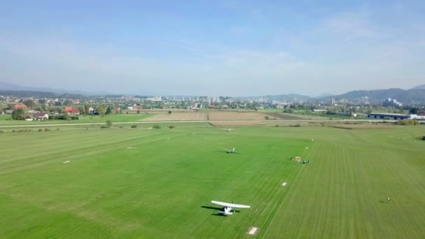 小さな白い飛行機がこの小さな空港を離着陸しています 緑の草の大きな畑があります 航空写真 — ストック動画