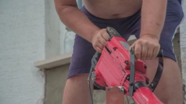 Sadece mavi şort giyen erkek işçi inşaat için beton yıkım çekici kullanıyor..