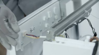 Tamirci, çamaşır makinesinin plastik ön panelini kaldırıyor. Sonra dikkatle elektrik kablolarını söker..