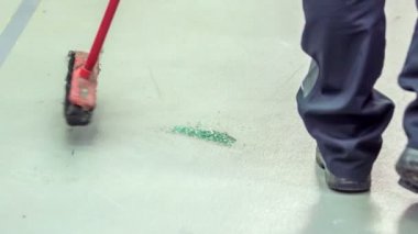 Genç bir tamirci bir otomobil tamirhanesinde yerleri tarıyor çünkü yerde yatan kırık pencerenin parçaları vardı..