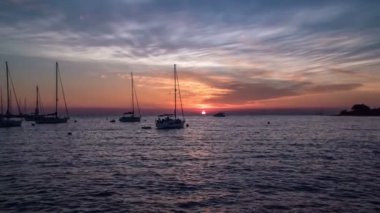 Many siling boats are standing on the sea and the sun is going down