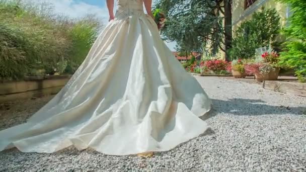 一位穿着漂亮的白色坐式连衣裙的年轻准新娘正走在一条狭窄的小路上 向正在等候她的新郎走去 她手里拿着一束漂亮的花束 — 图库视频影像