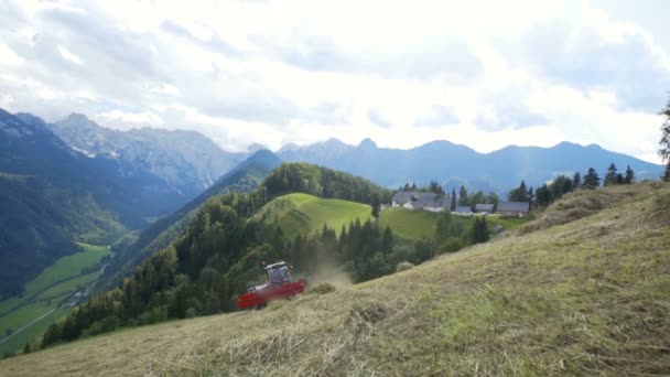トラクターは干し草を準備するために急な丘の上を運転しています 背景の壮大な眺め — ストック動画