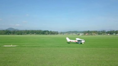 Küçük beyaz bir uçak yeşil bir çim üzerinde çalışıyor ve sadece küçük bir pervane hareket ediyor. Doğa çok güzel. Her şey yeşil. Havadan çekim.