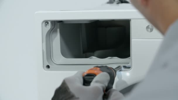 Reparaturarbeiter schrauben Schrauben des Gehäuses ab, in dem sich die Waschmittelschublade befindet. Er benutzt kleine Baterry-Bohrmaschine.