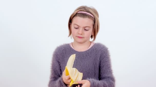 Ein Junges Mädchen Schält Eine Banane Und Beißt Dann Hinein — Stockvideo