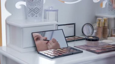 A young woman does her own make up in the make up studio and she applies a bit more make up on her lower eyelid.