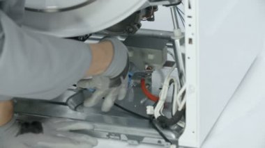 Tamirci ekstradan doğru hareket için eğri burun pensesi kullanıyor. Bozuk çamaşır makinesinden kısa şeffaf bir tüp çıkarıyor..