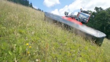 Traktör yokuş aşağı gidiyor ve tarım makineleri ile güzel yeşil çim kesiyor. Güzel bir yaz günü..