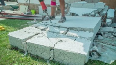 Güçlü kaya matkabıyla beton duvarı yıkıp küçük parçalara ayıran adam. Çok ciddi yaralandığı için dizinde bandaj var..