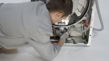 Genç adam vidaları özel bir aletle söküyor. Bozuk çamaşır makinesini tamir ediyor..