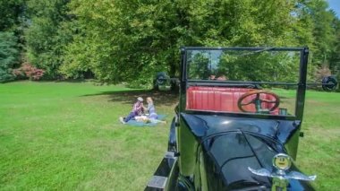 Güzel bir bahar gününde romantik anları birlikte geçirmek. Çift bir ağacın altında bir battaniye üzerinde oturuyor. Ayrıca yeşil çim üzerinde duran bir Vintage araba.