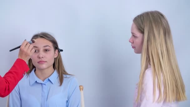 一位年轻女子安静地坐在化妆室的椅子上 化妆师在客户的额头上涂上一些液体粉末 — 图库视频影像