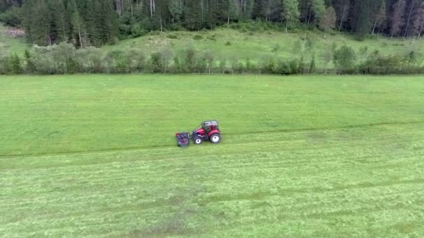 一辆红色的拖拉机正缓缓驶过田野 正在割草 空中拍摄 这是一个美好而温暖的夏日 — 图库视频影像