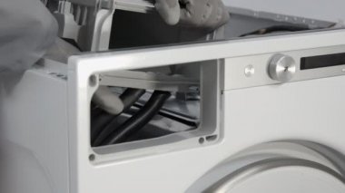 Tamirci dikkatlice su sağlayan lastik tüpleri kaldırıyor ve çamaşır makinesinin deterjan çekmecesine bağlanıyor..