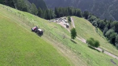 Bir traktör yazın saman hazırlarken dikkatli bir şekilde yokuş yukarı sürmektedir. Tepenin eteğinde güzel bir çiftlik var..