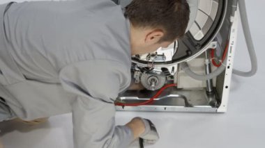 Genç adam uzun vidayı bozuk çamaşır makinesinin arka tarafından söküyor..