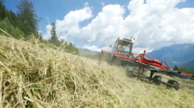 Bir çiftçi traktörünü çim tarlasında sürerken tarım makinelerindeki büyük tırmıklar hızlı hareket ediyor..