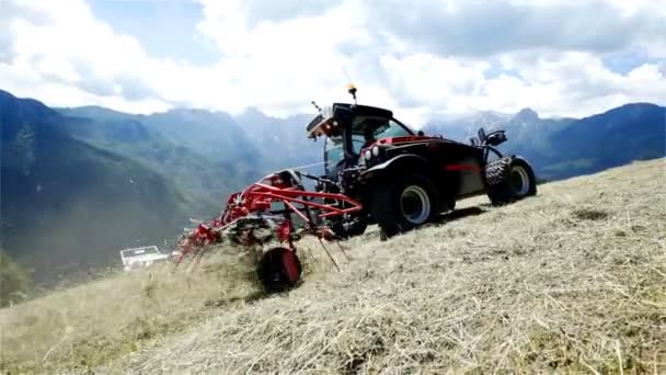 一辆拖拉机在山上行驶 农业机械正在组织干草 白天阳光明媚 后面景色令人叹为观止 — 图库视频影像