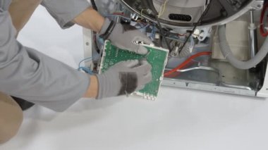 Tamirci çamaşır makinesini yöneten elektronik devreyi kaldırıyor. Küçük tornavidalara yardım ediyor..