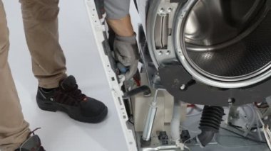Tamirci bozuk çamaşır makinesinin yanındaki elektrik kablolarını söküyor..