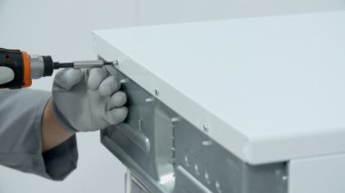 Çamaşır makinesinin üst kısmını tutan vidaları söken adam.