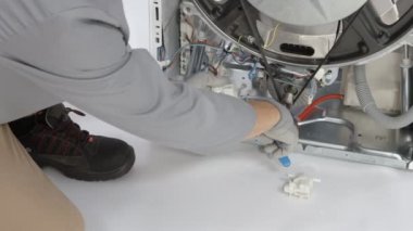 Tamirci, bozuk çamaşır makinesinin beyaz plastik kısmından dar hortumu ayırıyor. Tamirci iğneli burun pensesi takmaya yardım ediyor..