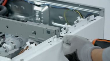 Tamirci çamaşır makinesinin yan tahtalarını tutan vidaları söküyor..