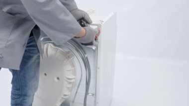 Bir adam çamaşır makinesinden vida ları çıkarıyor ve matkap kullanıyor..