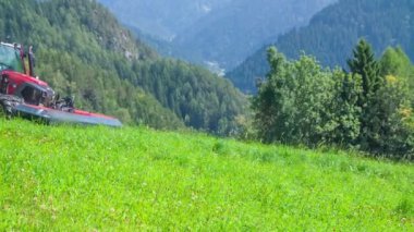 Bir çiftçi güzel bir yeşil tepede yokuş aşağı sürüş ve o çim kesme makineleri ile çim kesiyor. Gün güneşli ve sıcak.