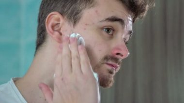 Genç bir adam yavaşça sola ve yüzünün sağ kısmına tıraş köpüğü koyuyor..