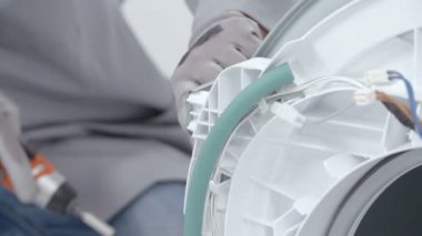 Bir adam bir çamaşır makinesi tamir ve şu anda, o bir matkap kullanarak vida çıkarıyor.