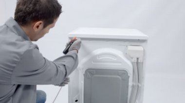 Bir tamirci çamaşır makinesinin arka vidalarını çıkarmak için matkap kullanıyor. Bunu düzeltmesi gerek..