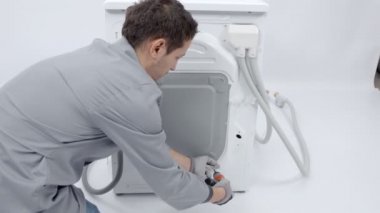 Bir tamirci arka kapıyı çamaşır makinesinin kapısını açıyor. Vidaları çıkarmak için matkap kullanıyor..