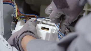 Bir adam küçük bir aletin tüm kablolarını çıkarmaya çalışıyor. Güvenlik eldiveni kullanıyor..