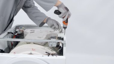 Bir tamirci matkapla vidaları çıkarıyor. Çamaşır ve kurutma makinesini tamir ediyor..