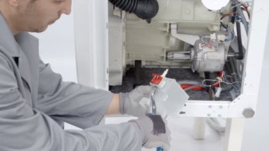 Bir adam çamaşır makinesiyle ilgili bir sorunun nerede olduğunu bulmaya çalışıyor. Tamir ediyor..