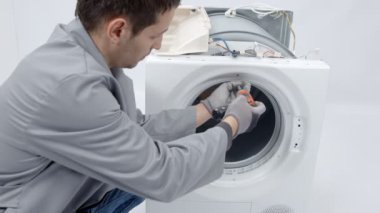 Bir adam küçük vidalar çıkarıyor ve o bir matkap kullanıyor. Çamaşır ve kurutma makinesini tamir ediyor..