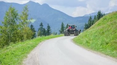 Bir traktör ülke yolda gerçekten hızlı sürüyor ve o yokuş yukarı gidiyor. Gün güneşli ve çiftçilerin açık havada çok iş var yaz saati. Saman hazırlıyorlar..