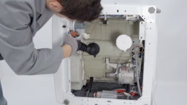 Bir tamirci bütün bir çamaşır makinesini parçalara ayırıyor ve farklı aletlerle tamir ediyor..