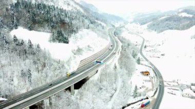 Viyadük üzerindeki bir otoyol ve viyadük altındaki bir yol paralel çalışıyor. Kış zamanı ve doğa karla kaplı. Gün bulutlu. Havadan çekim.