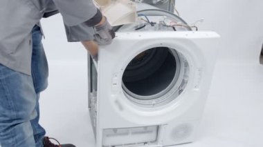 Bir tamirci çamaşır makinesinin ön tarafını tamir ediyor. Sorunu çözebilmek için tüm cihazı sökmesi gerekiyor..