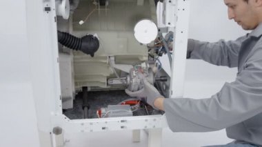 Bir tamirci çamaşır makinesini tamir etmek için tornavida kullanıyor. Zaten tüm cihazı parçalara ayırdı..