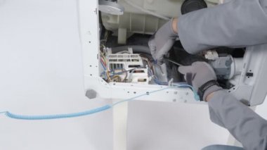 Bir adam çamaşır makinesini tornavidayla tamir ediyor. Farklı aletler kullanıyor..