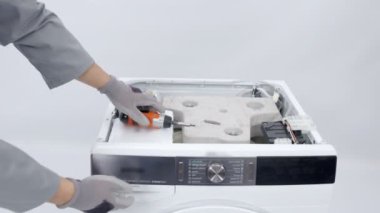 Bir tamirci çamaşır makinesinden bir dağıtıcı alıyor. Cihazı sökecek çünkü bir şeyleri düzeltmesi gerekiyor..
